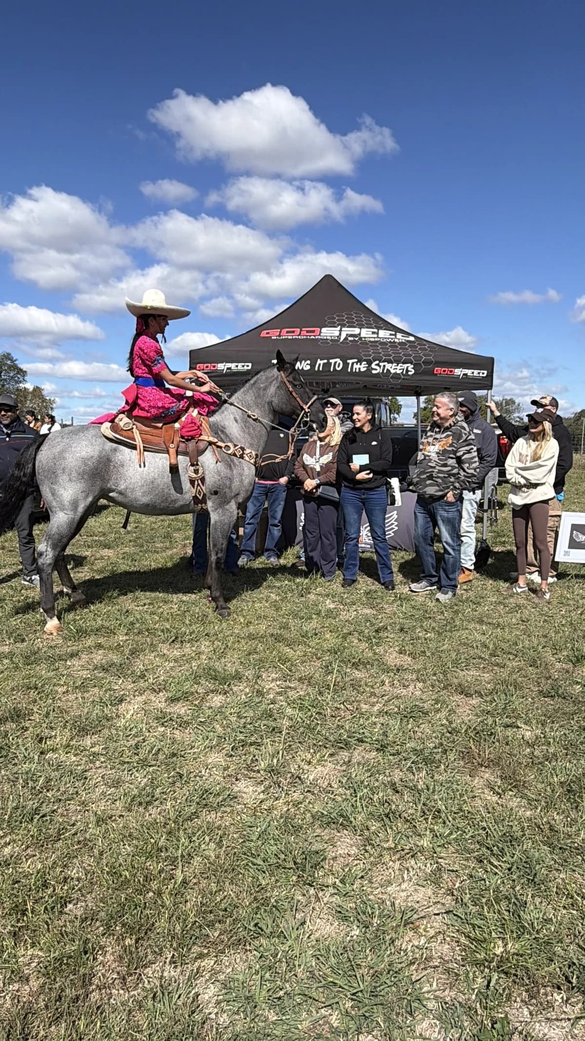 Jackie Jaramillo on a blue roan horse beside a black tent, guests standing in a line to watch