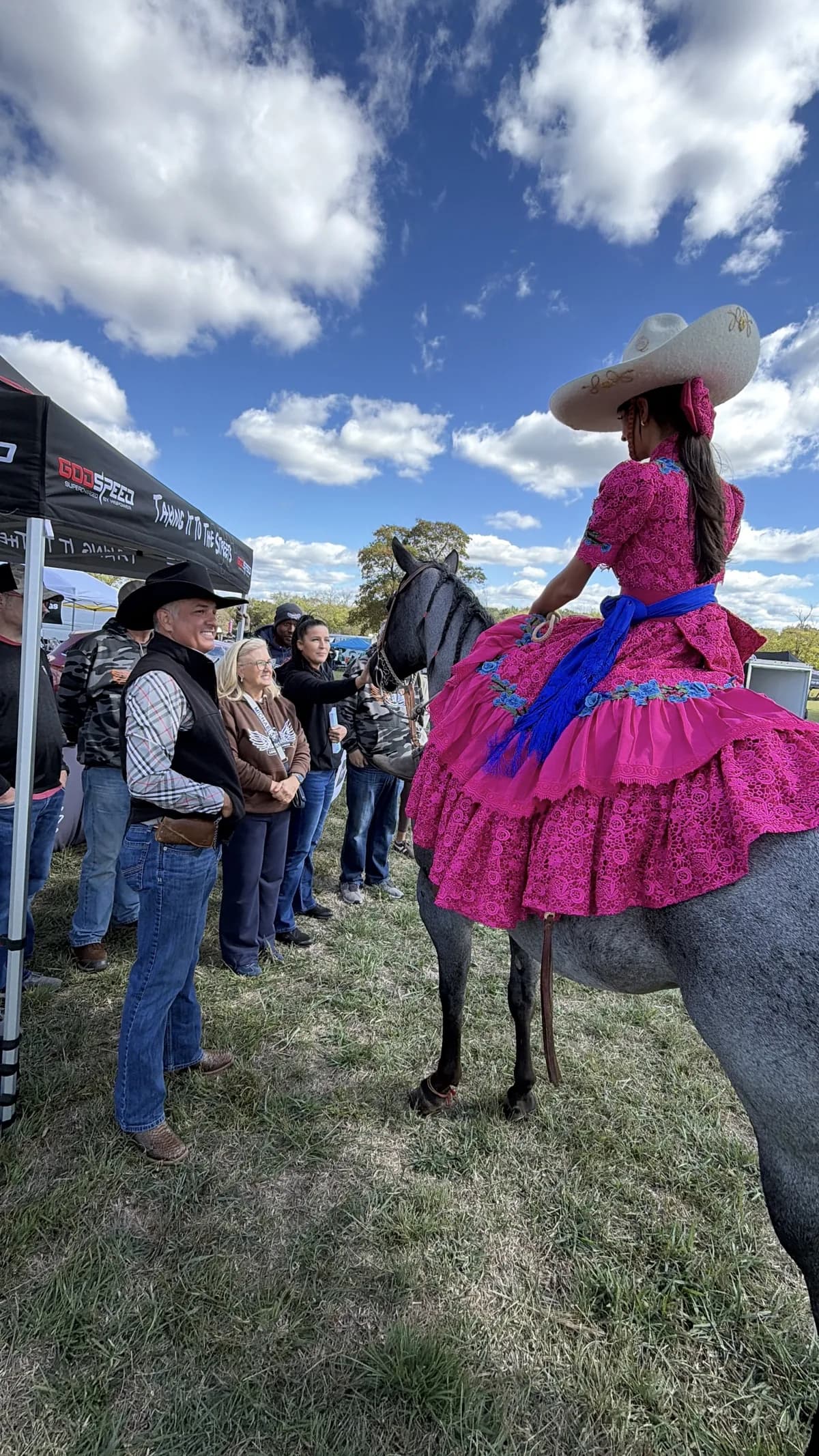 Jackie Jaramillo seen from behind on her horse, the pink escaramuza dress and blue sash spread over its back