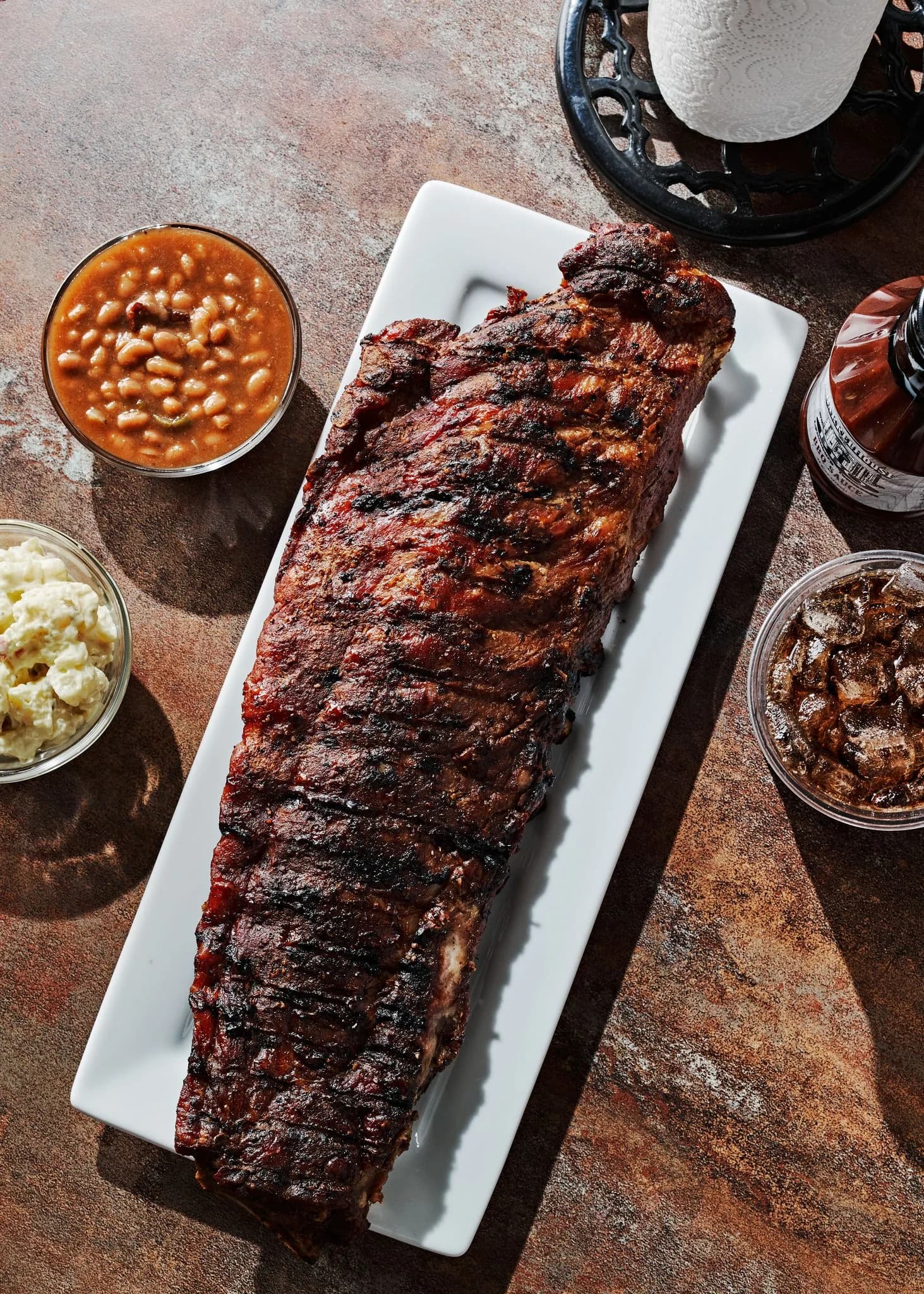 A full rack of ribs on a white platter, seen from above, with baked beans and potato salad