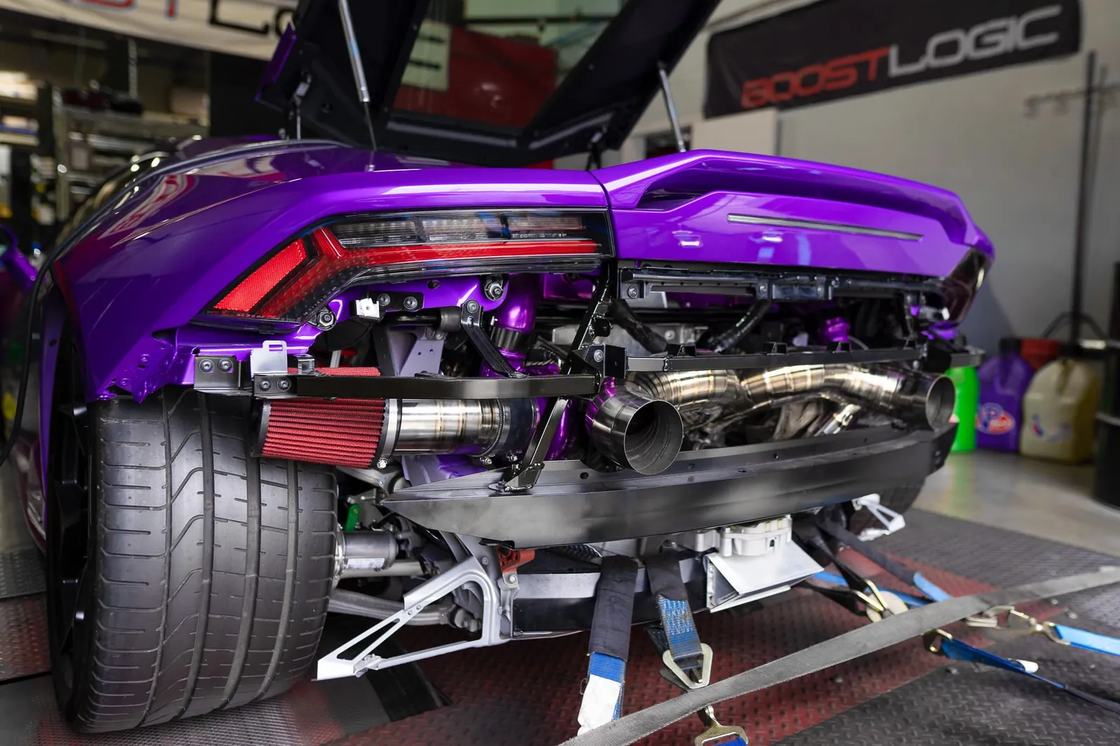 A purple Lamborghini Huracán on the dyno in Boost Logic's shop, its rear bumper off and the twin turbos showing, a BOOSTLOGIC banner on the wall
