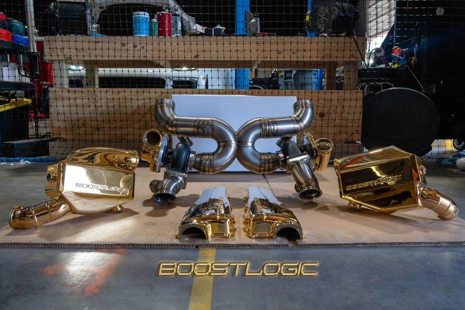 A gold-plated Boost Logic twin-turbo kit laid out on the shop floor with its intercoolers and titanium pipes