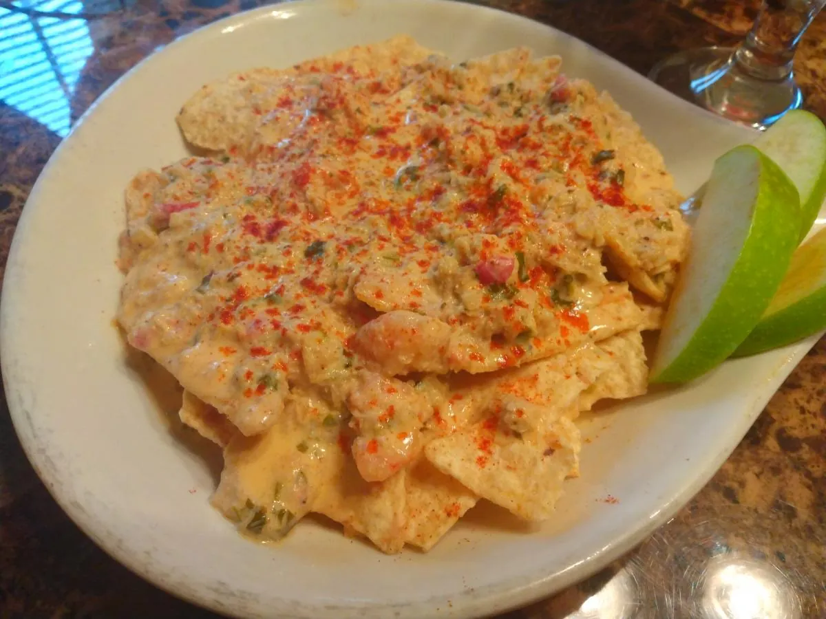 A plate of tortilla chips under a creamy shrimp sauce, with green apple slices and a lemon wedge beside it