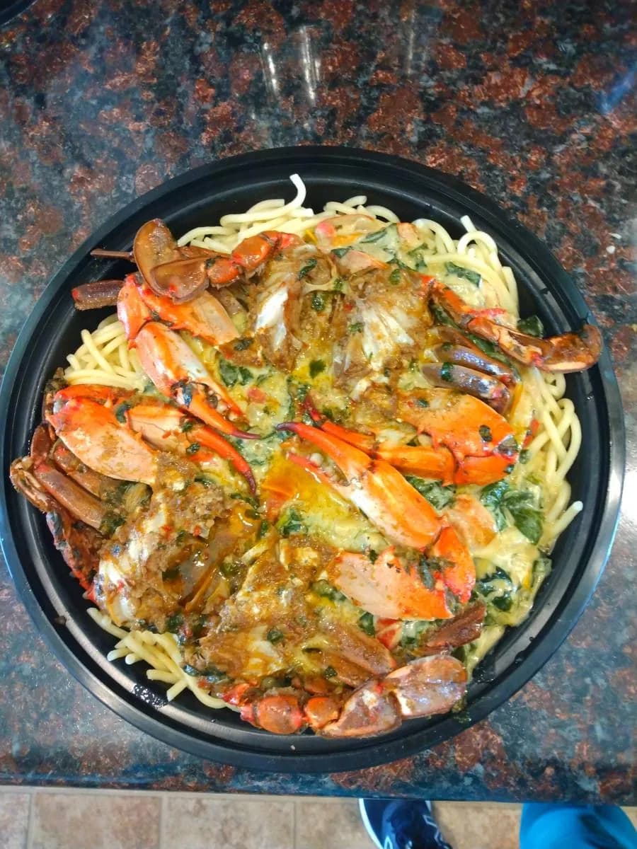 Blue crab over linguine in a spinach cream sauce, in a black tray on a granite counter