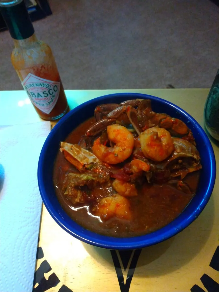 Shrimp and crab stew in a blue bowl, a bottle of hot sauce beside it
