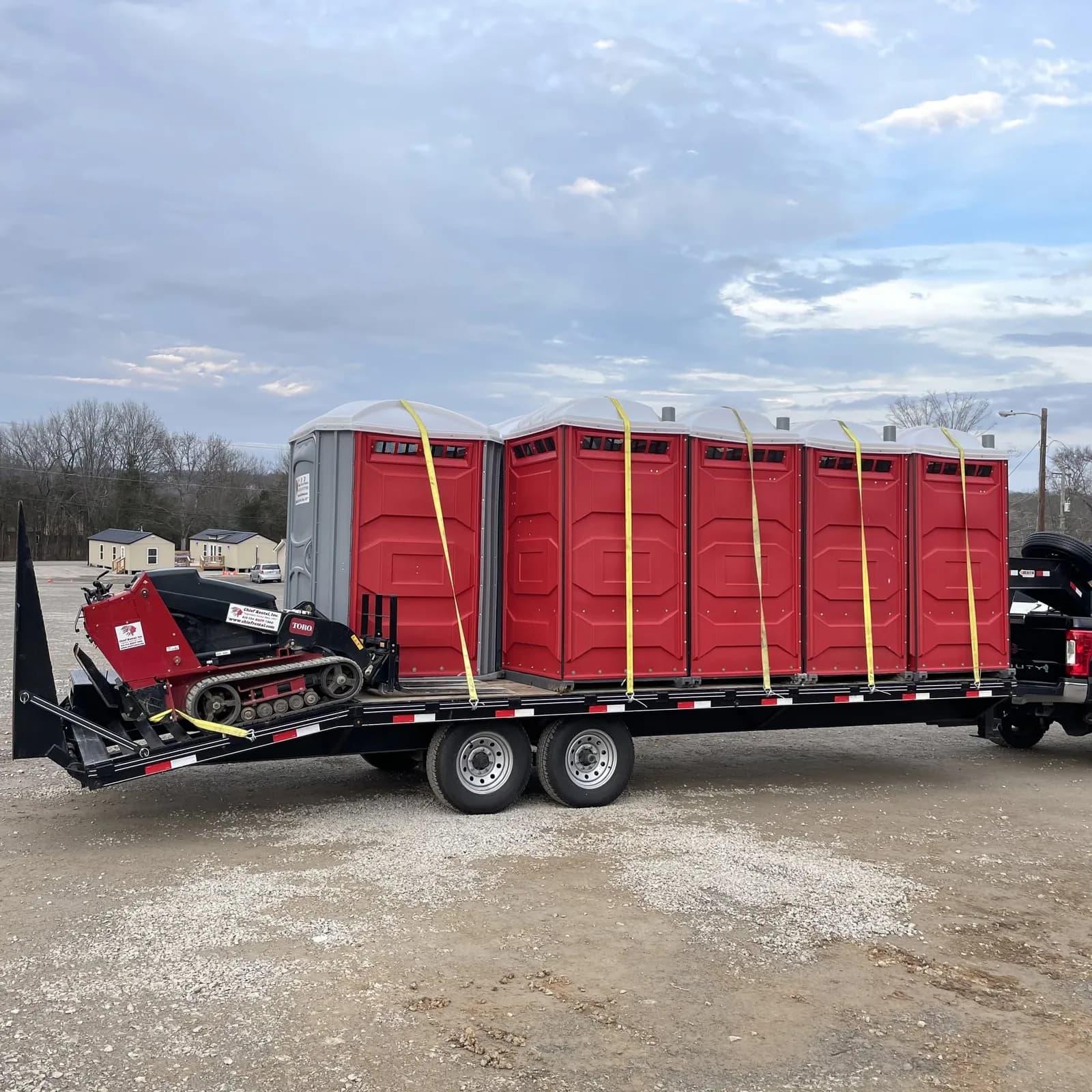 Red portable restrooms strapped down on a flatbed trailer, ready to deliver