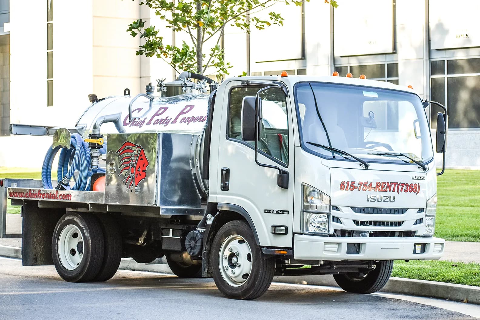 A white Chief Party Poopers pump truck with its tank and hoses, parked on a lawn