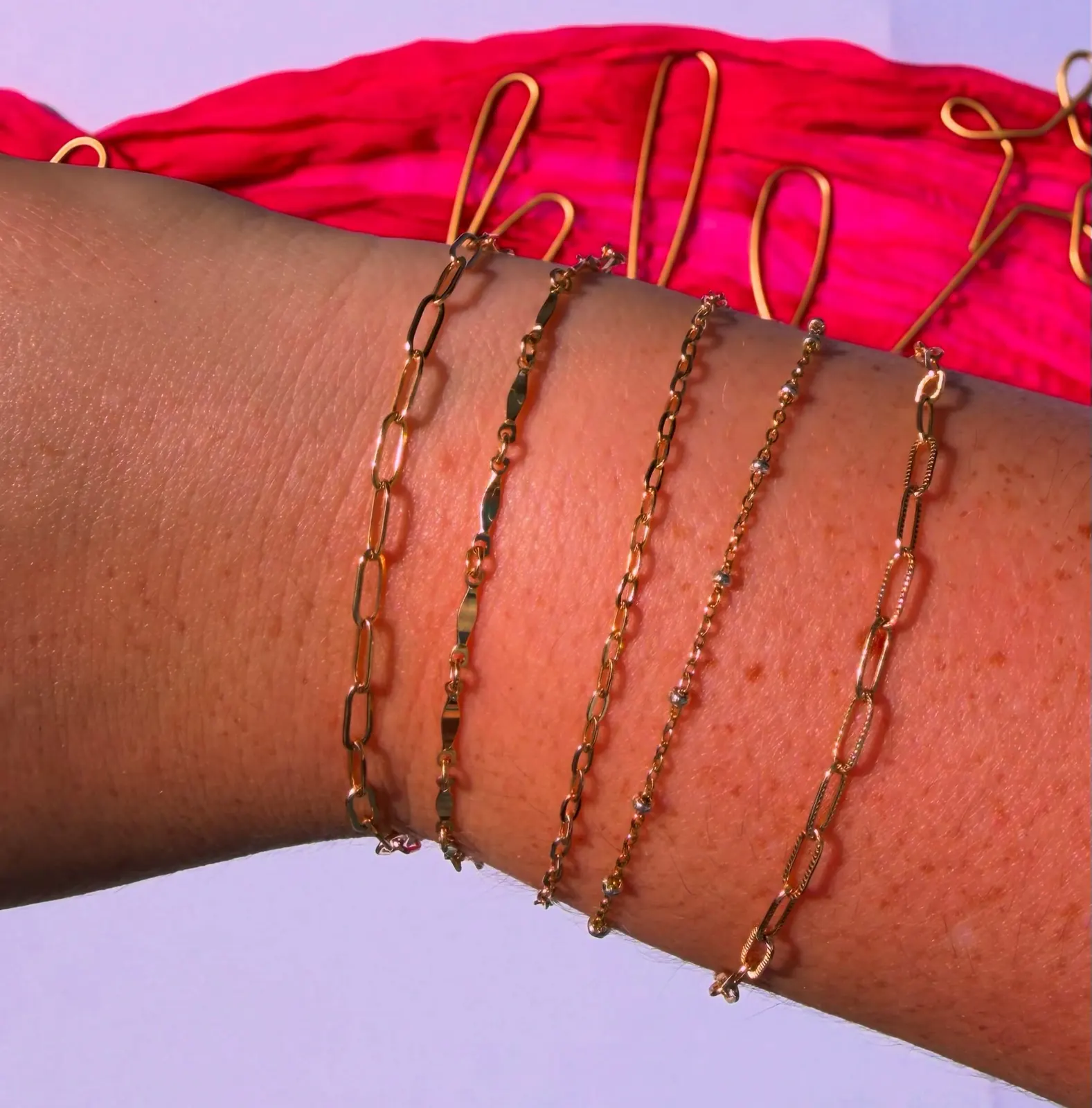 Five gold chain bracelets, in paperclip, bar, cable and bead styles, worn on one wrist