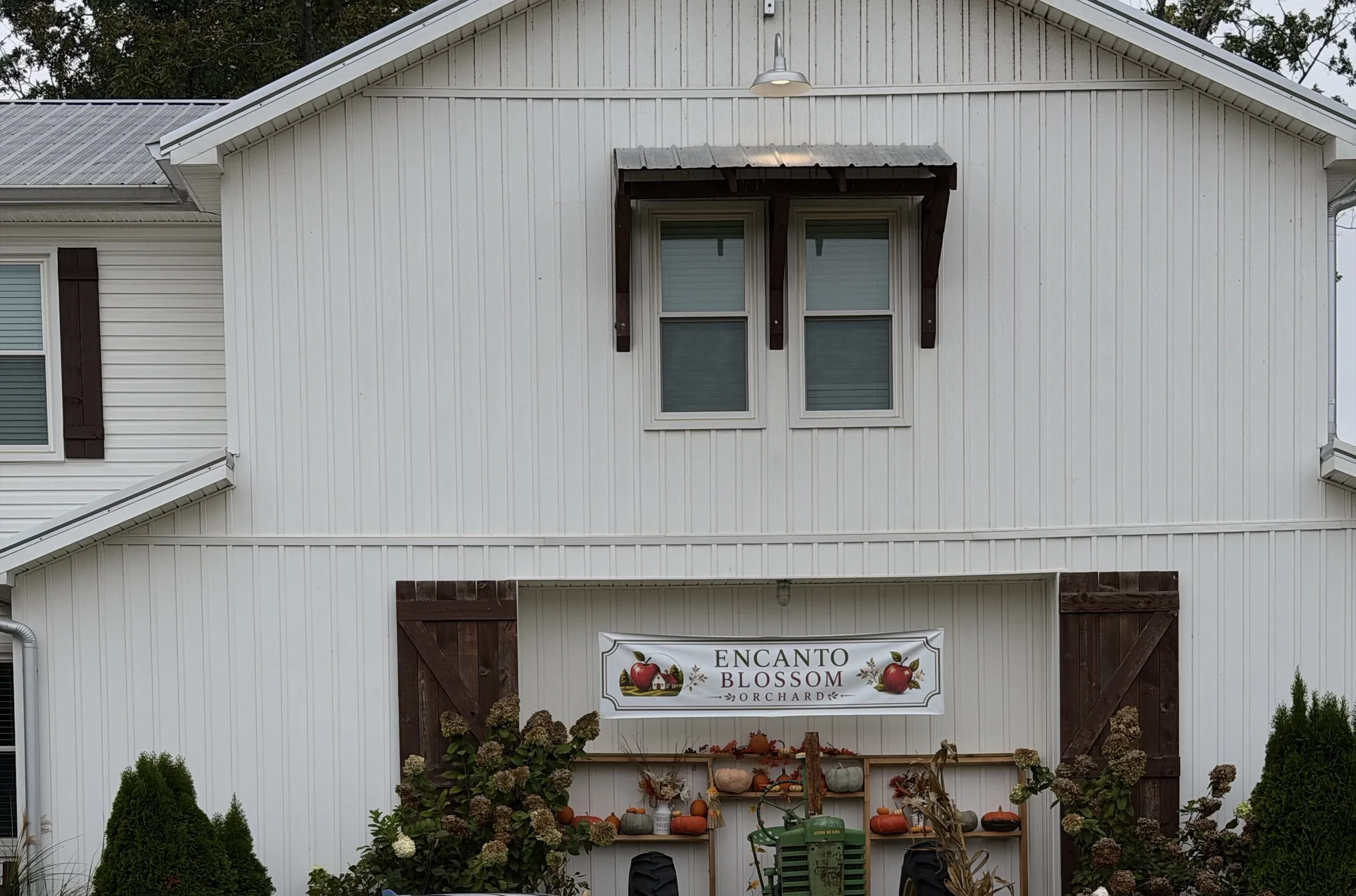 The Encanto Blossom Orchard banner on the white farmhouse wall, between two dark barn doors, over shelves of fall decorations