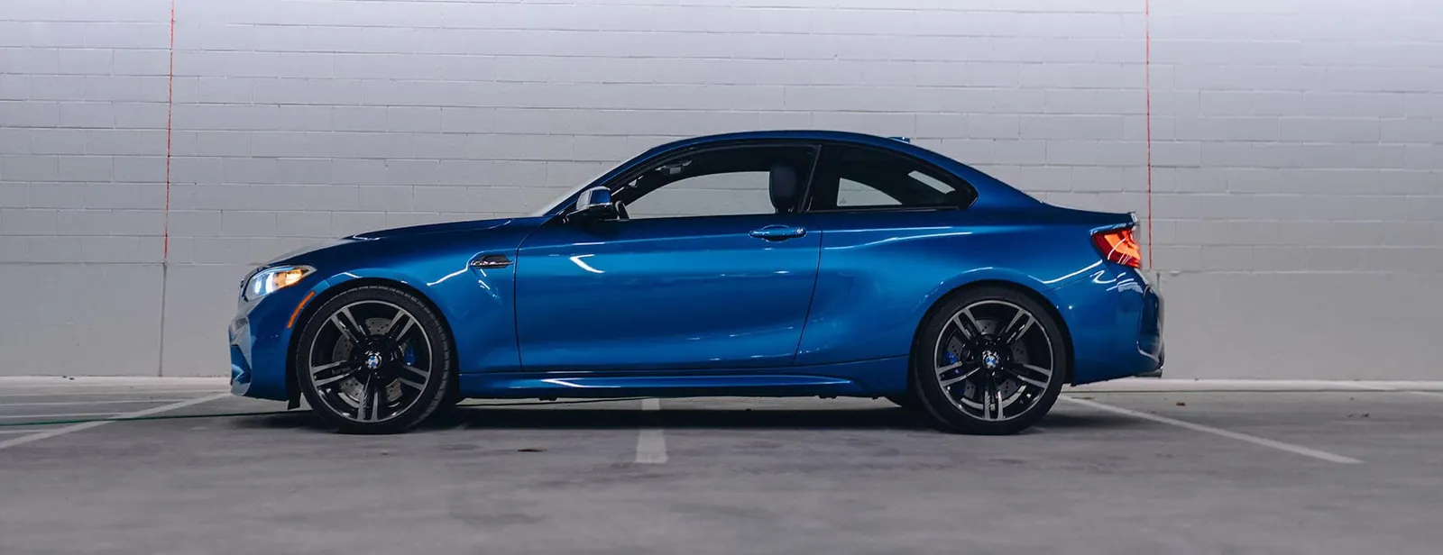 A blue BMW M2 coupe in profile against a white wall