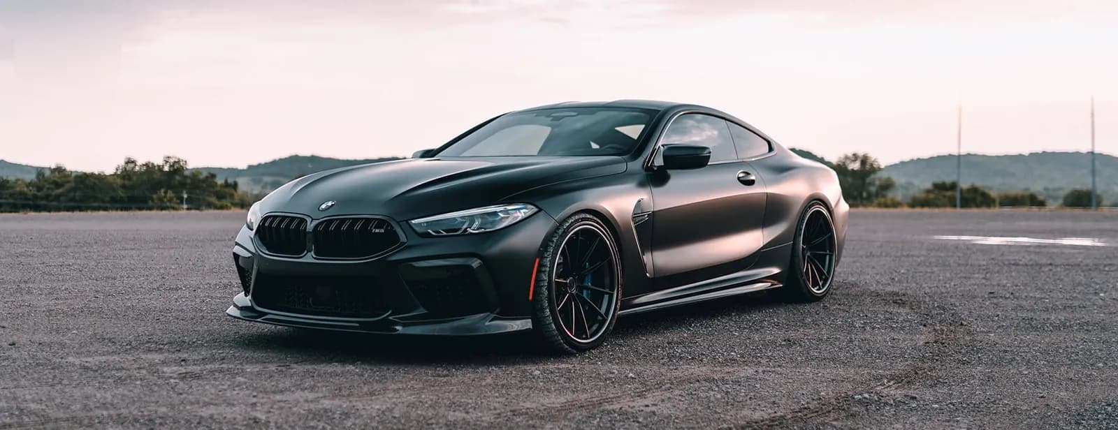 A dark matte BMW 8 Series coupe on an open gravel lot