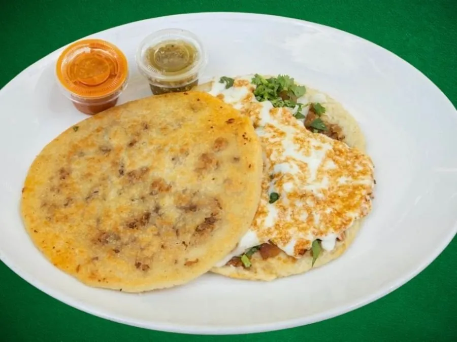 A golden pressed gordita beside a cheese topped tortilla on a white plate, with two salsa cups