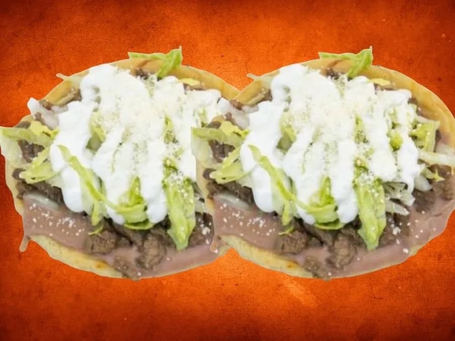 Two sopes topped with steak, lettuce, cream and crumbled cheese on an orange ground
