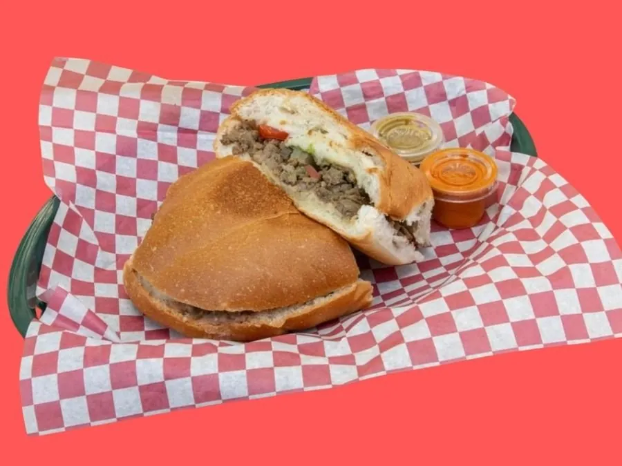 A steak torta cut in half on a red and white checkered liner, with two salsa cups