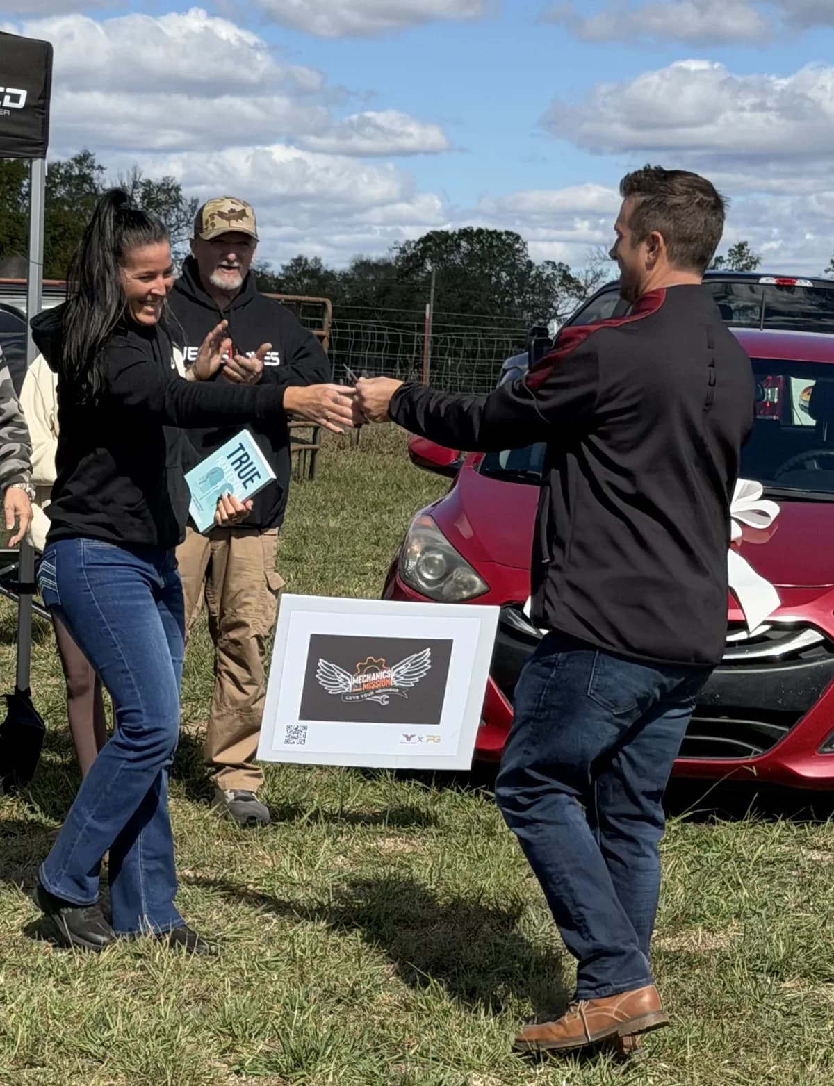 The car presentation at the Mechanics on a Mission tent, people smiling as something is handed over