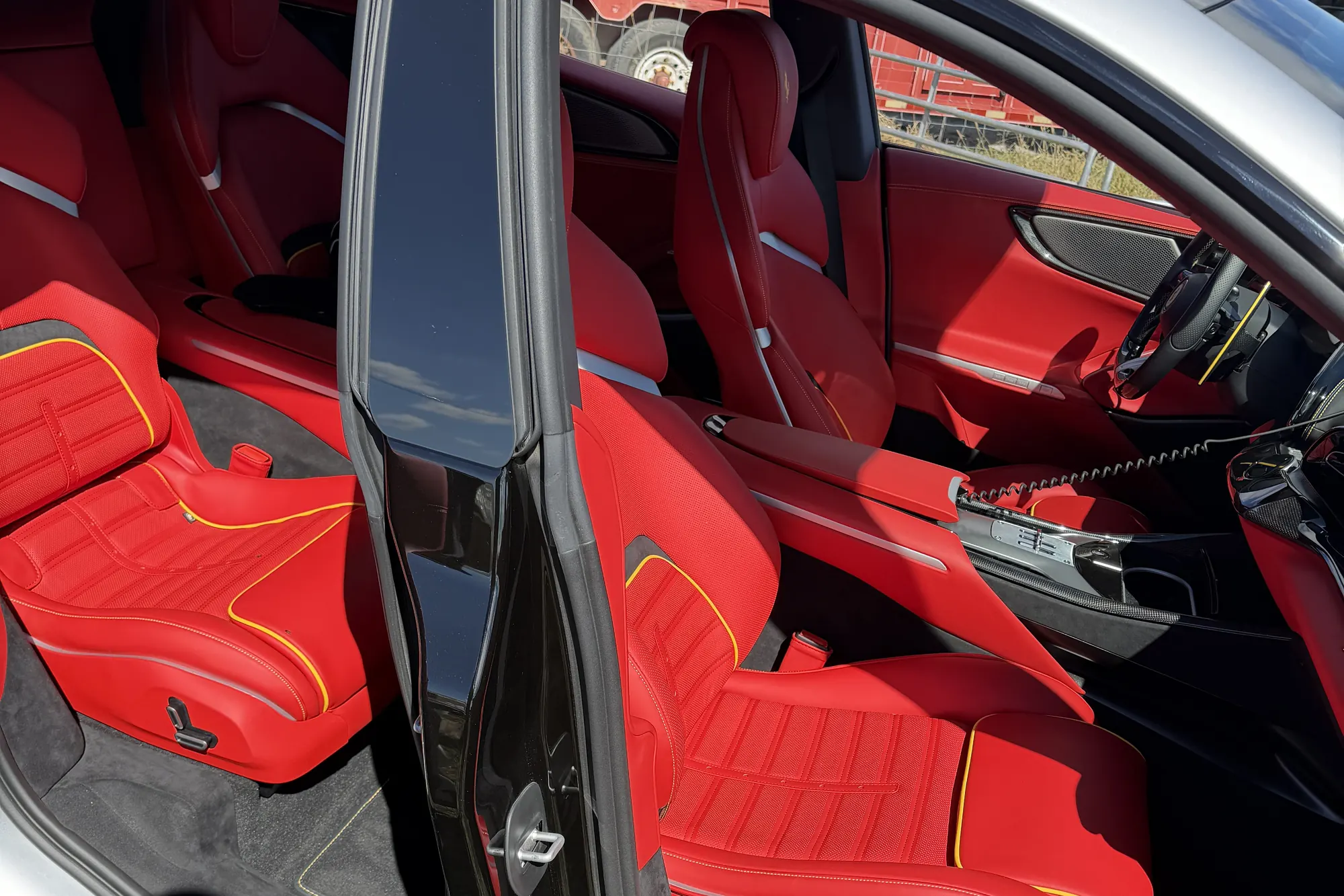 A silver Ferrari Purosangue at the ranch with its doors open, red leather seats with yellow stitching inside