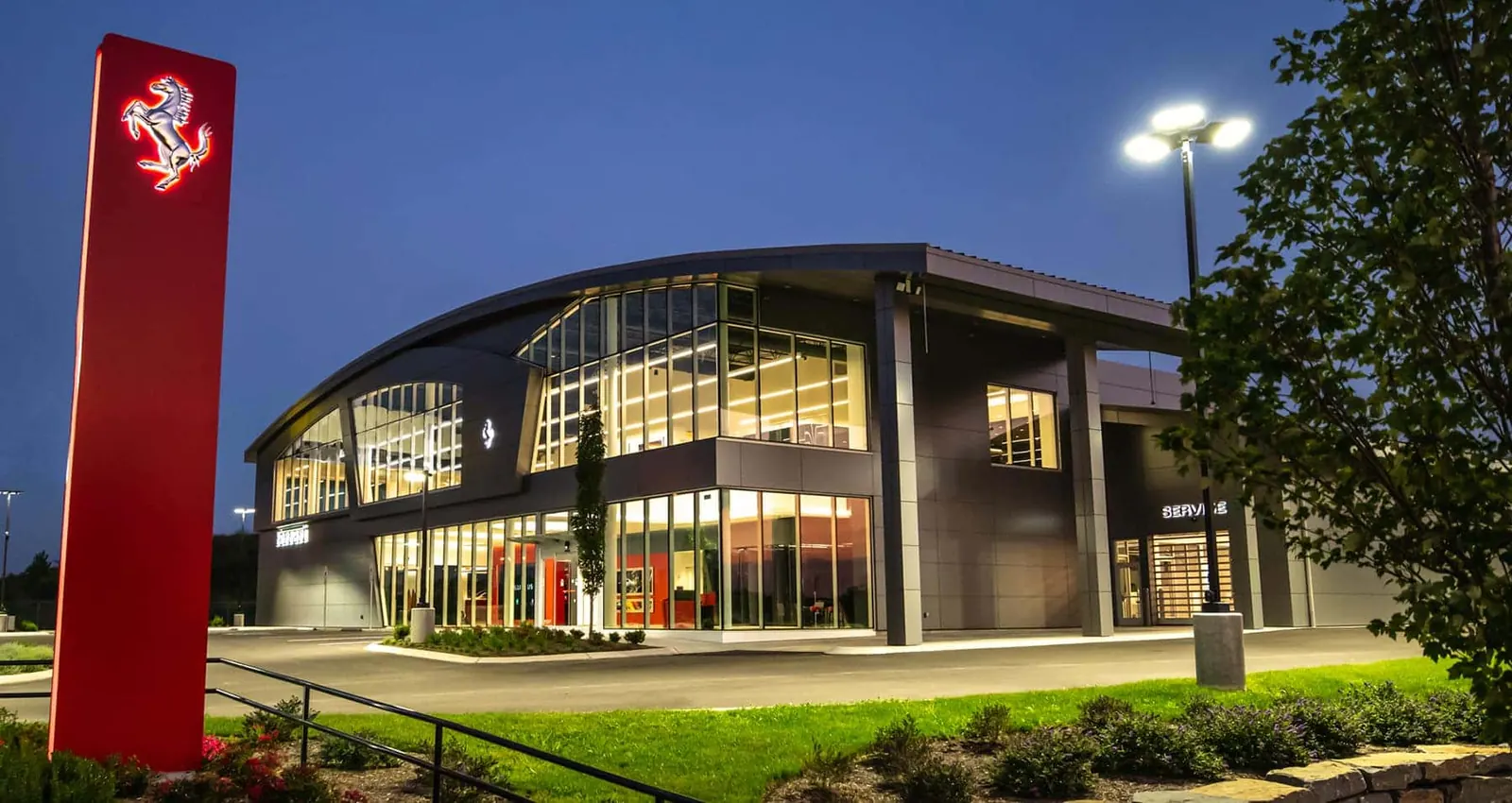 The Prancing Horse of Nashville dealership at dusk, its showroom lit and a red Ferrari sign out front