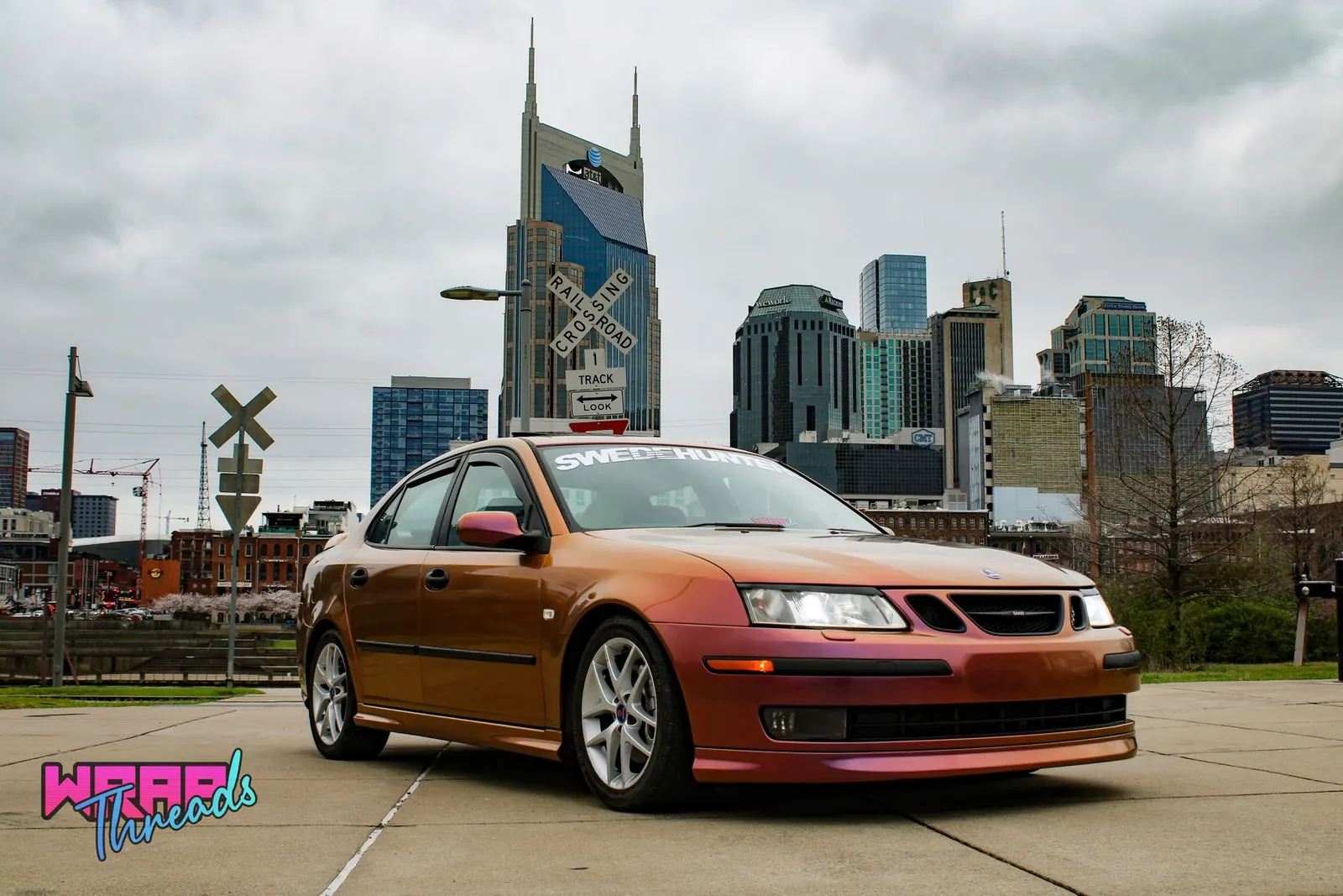 A color-shift orange and purple Saab parked with the Nashville skyline behind it