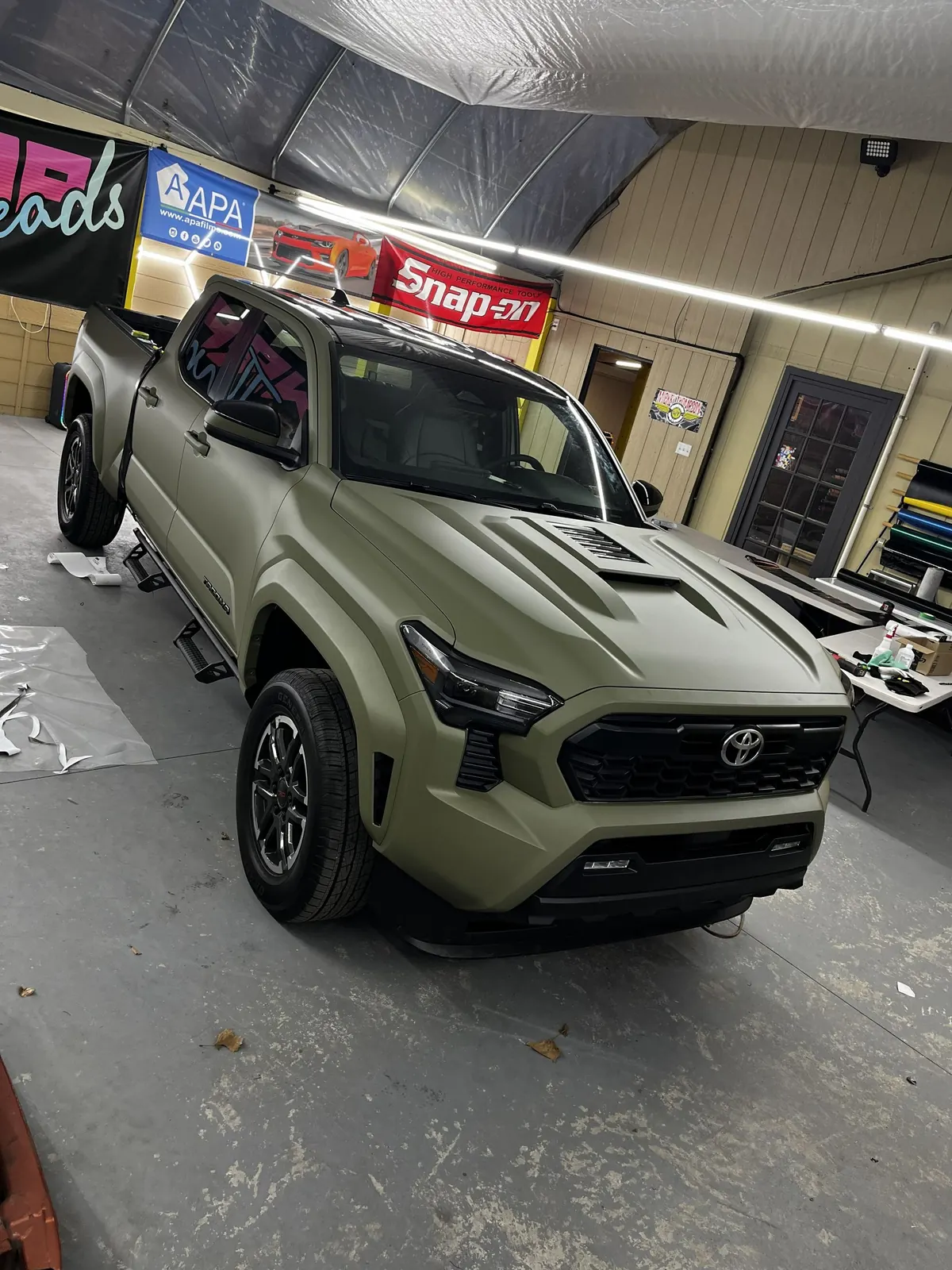 An olive Toyota Tacoma part way through a wrap in the shop