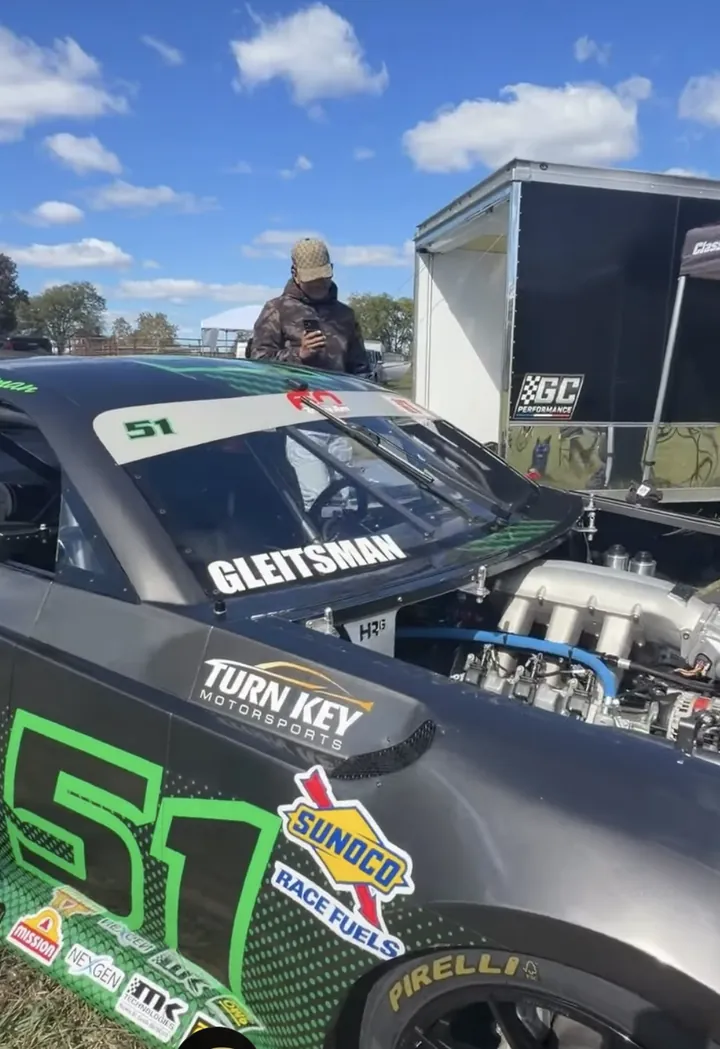 A frame from the recap reel: the number 51 race car with its hood up beside the GC Performance trailer, a guest filming it on a phone