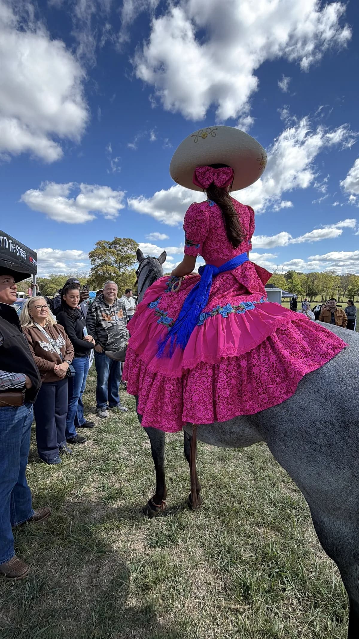 Jackie Jaramillo on her horse, seen from behind, her dress spread over its back, guests watching beside a black tent