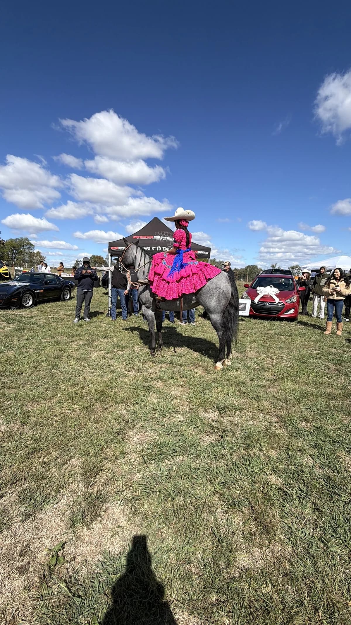 Jackie Jaramillo riding toward the camera across the show field, cars and guests behind her