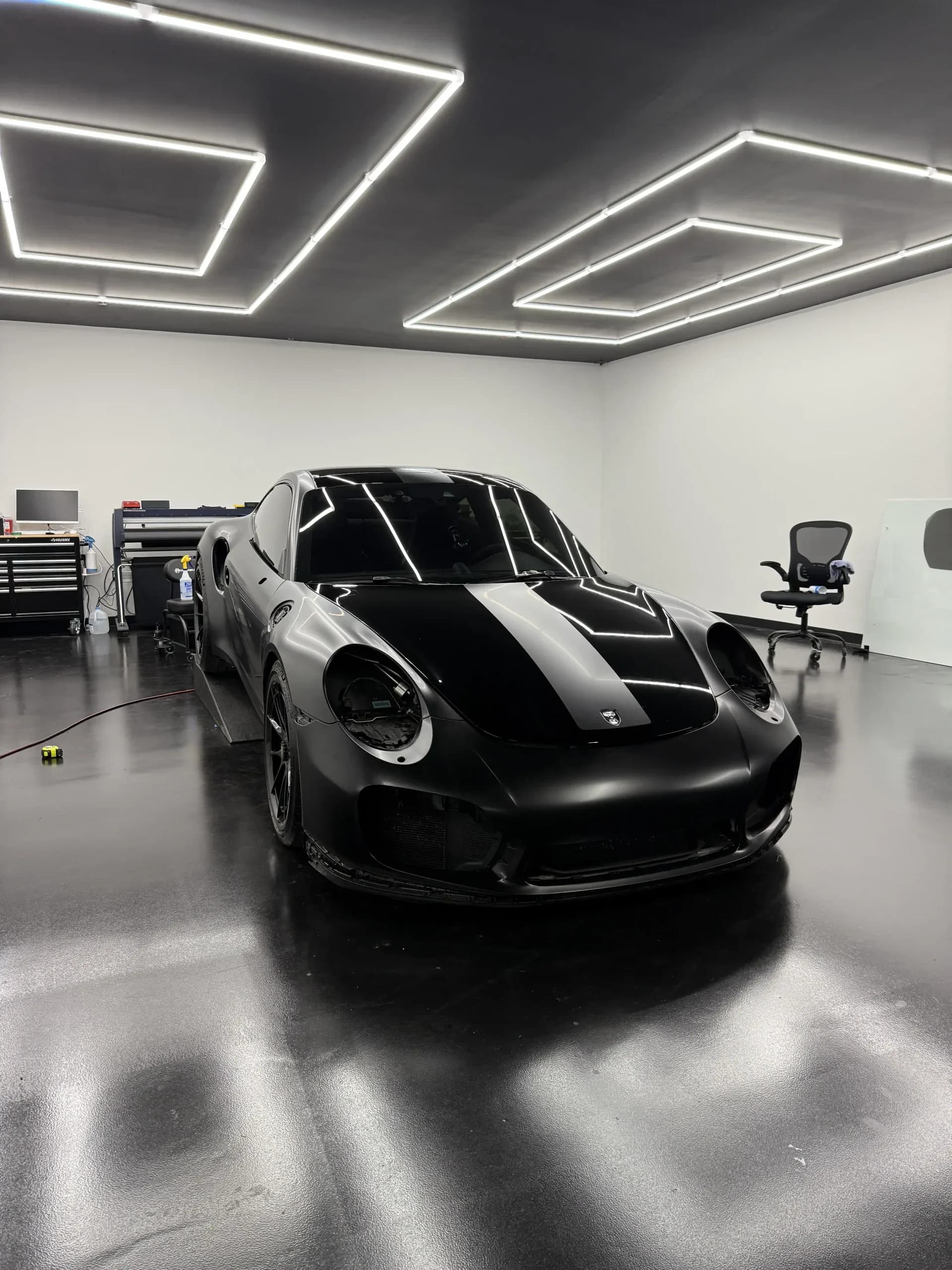 A black Porsche 911 with a satin stripe in La Cueva's studio, square light panels on the ceiling and a gloss floor